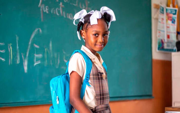 Cómo incluir a UNICEF en tu testamento y ayudar a los niños en el futuro Una niña en una clase con mochila de UNICEF