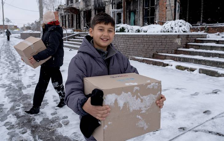 Artur lleva una caja con ropa de invierno, recibida en el punto de distribución de UNICEF. Artur de 9 años
