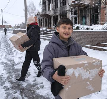 Artur lleva una caja con ropa de invierno, recibida en el punto de distribución de UNICEF. Artur de 9 años