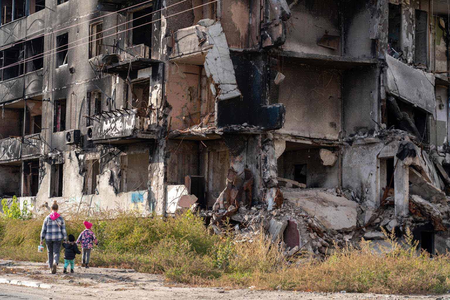 UN0765276 Filippov Una madre y dos niños ucranianos caminando al lado de un edificio en ruinas