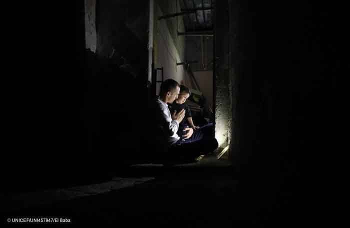 Un padre abraza a su hija en la completa oscuridad de la noche, en su casa sin electricidad en Gaza