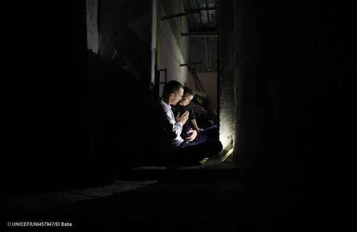 Un padre abraza a su hija en la completa oscuridad de la noche, en su casa sin electricidad en Gaza