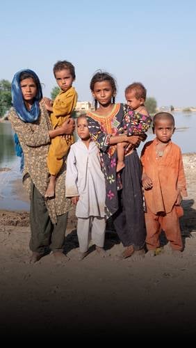Unos niños frente a un charco de agua estancada.