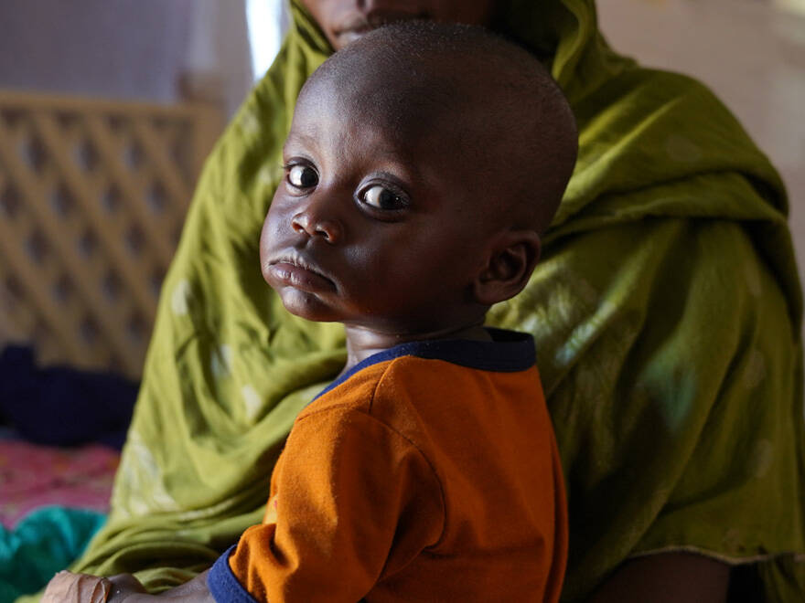 Un niño espera a ser atendido en un centro de nutrición de UNICEF en Abushok, Sudán. Un niño en brazos de su madre