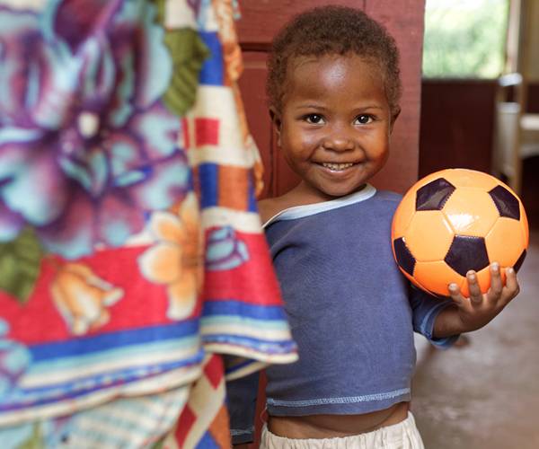 Con la colaboración de personas como tú, Jean pudo nacer en un hospital apoyado por UNICEF y, tanto él como su madre, seguir recibiendo revisiones periódicas. Un niño sonríe mientras sostiene un balón de futbol