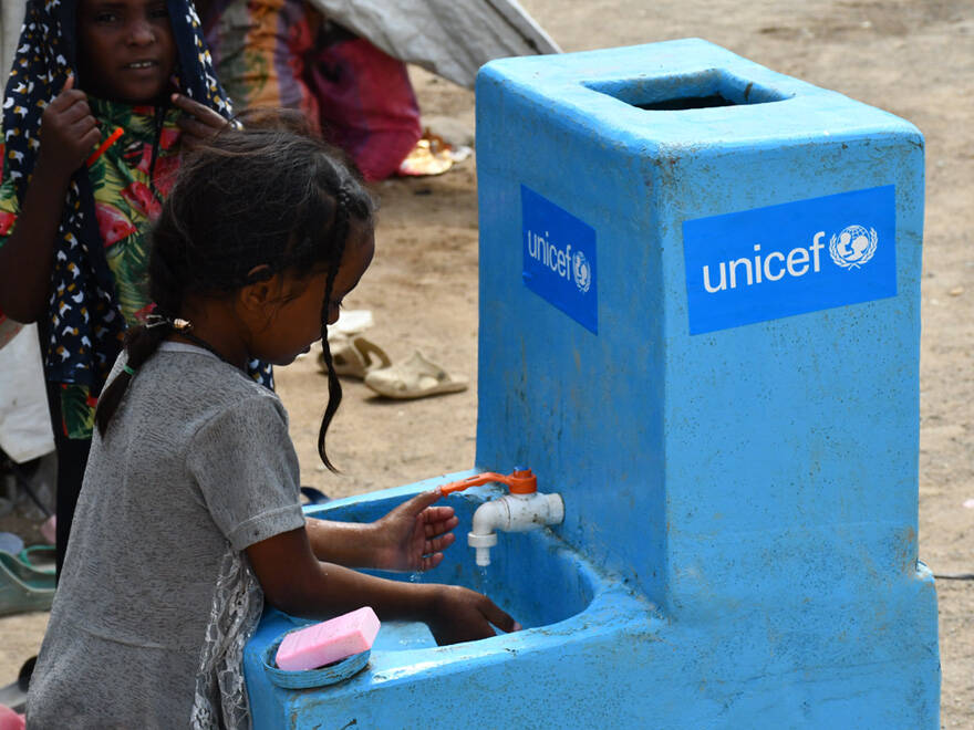 Una niña coge agua en una fuente instalada en un espacio seguro para niños por UNICEF. una niña coge agua