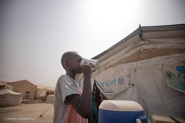 Un niño desplazado por el clima bebe agua frente a una tienda instalada por UNICEF