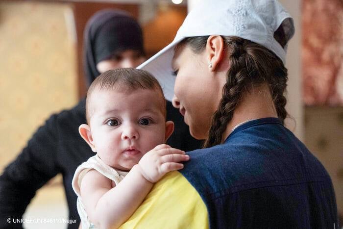 Una trabajadora nutricional de un equipo móvil apoyado por UNICEF sostiene a Samar, de 5 meses, y la prepara para un control de peso