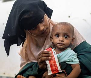 Una madre rohingya recién llegada alimenta a su hijo con un paquete de alimentos nutritivos. Una madre rohingya recién llegada alimenta a su hijo con un paquete de alimentos nutritivos.