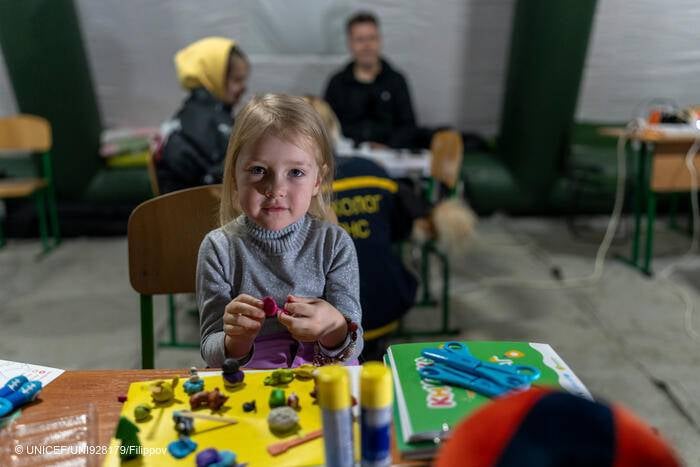 Arina, de tres años, está sentada a una mesa jugando con plastilina dentro de una tienda móvil de emergencia