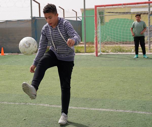 En un campo de refugiados, Anwar encontró un espacio seguro donde volver a jugar, aprender y sentirse niño gracias a UNICEF y su red de apoyo. Un niño juega con un balón de futbol