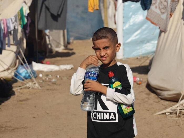 Un niño posa con una botella de agua y un producto de limpieza en la mano